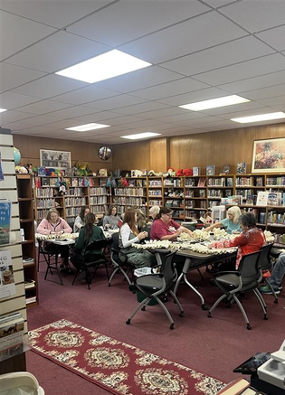 Group of older adults sitting at tables in library working on a craft project